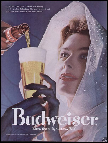 This 1957 Budweiser ad shows a woman in virginal white looking up at her male beer provider. A bit submissive, no? 
